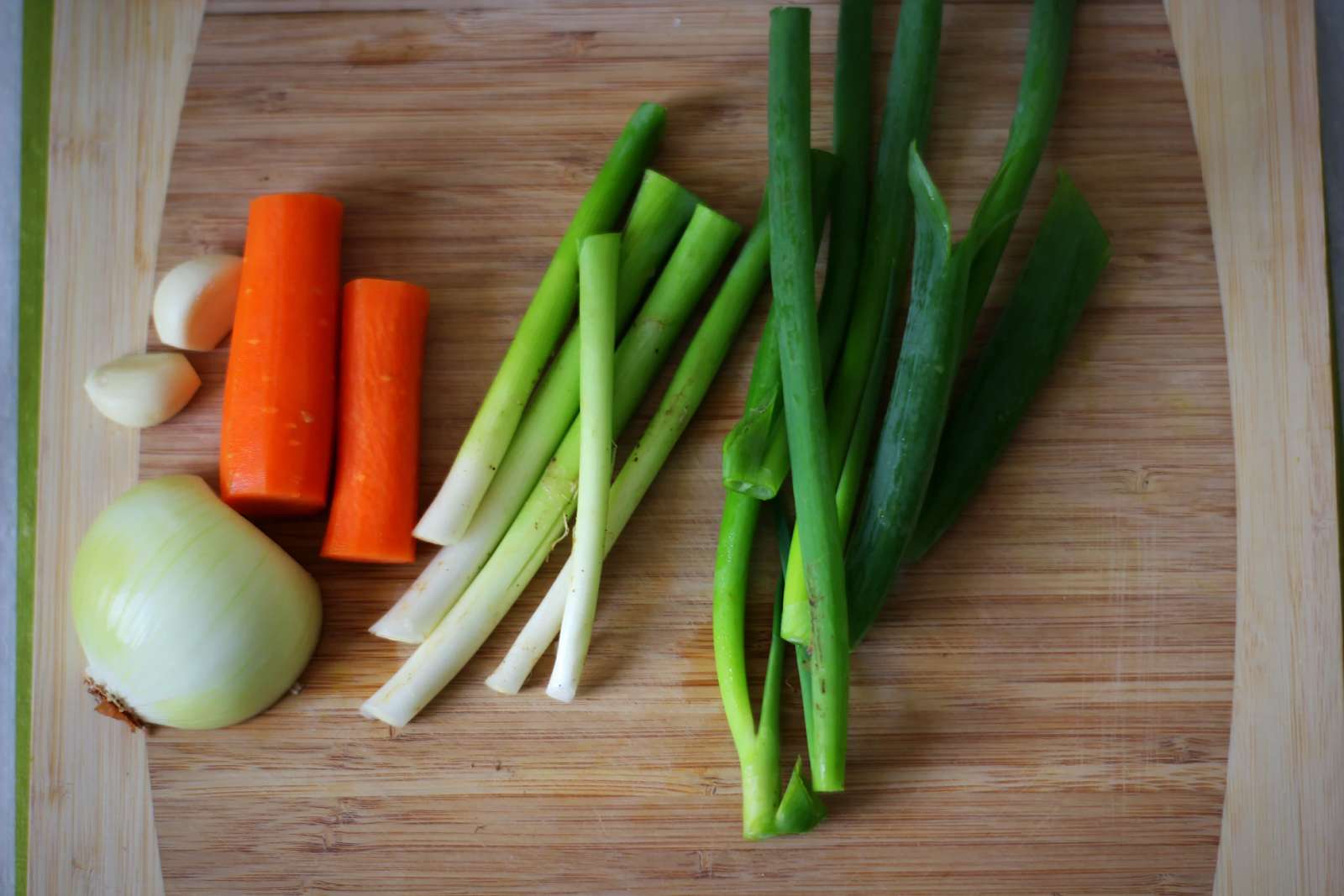 Onions, garlic, carrots and green onions on a wooden cutting board.