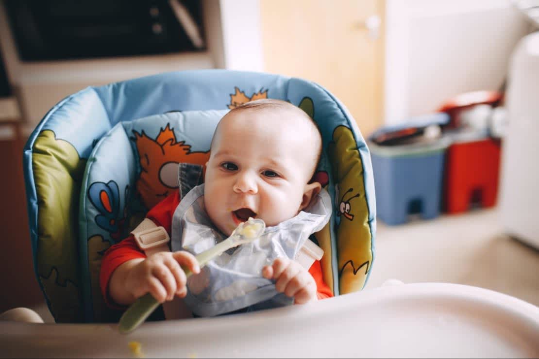 Caucasian baby in highchair feeding themselves with a spoon 