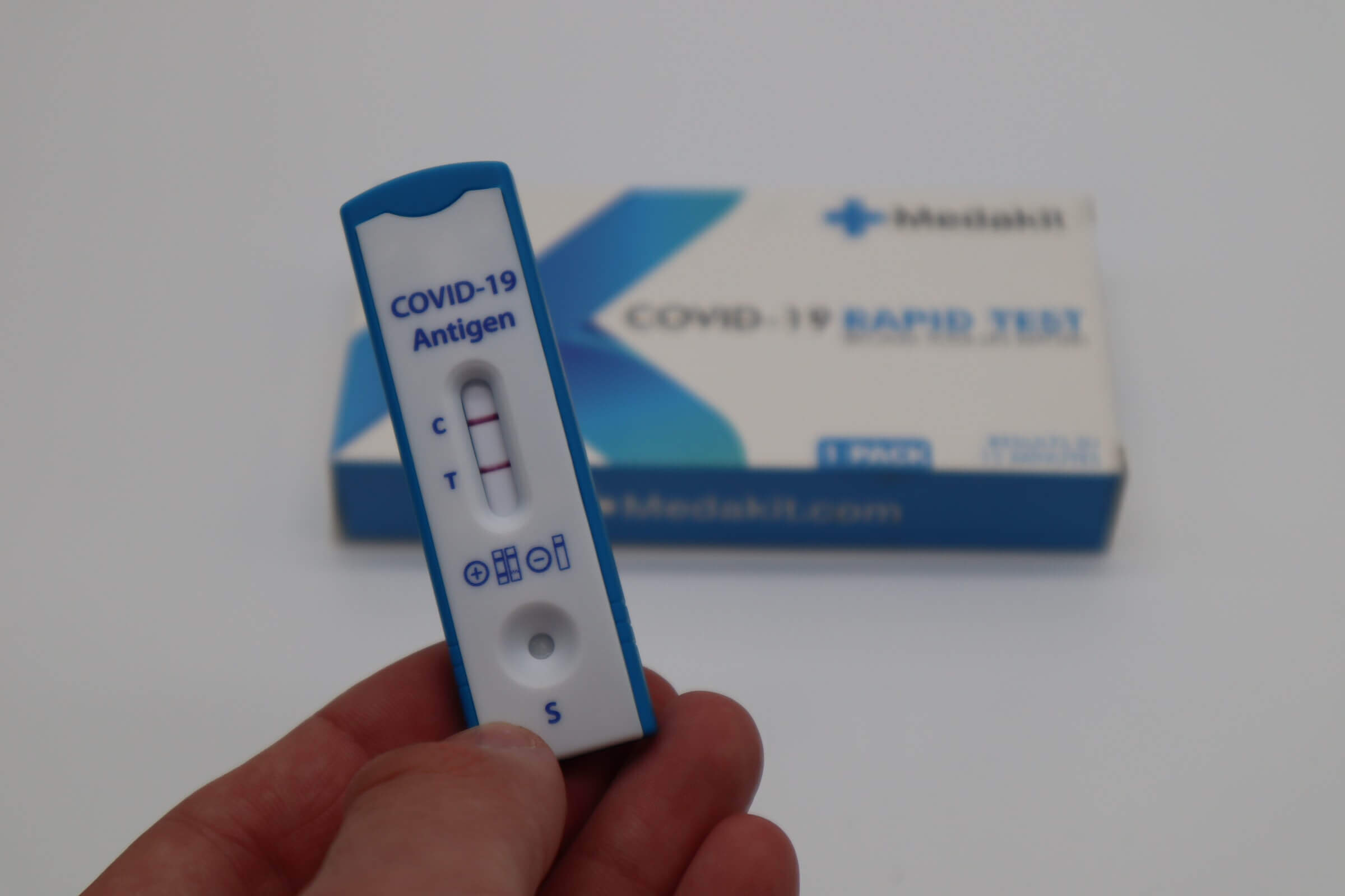 Person holding rapid covid antigen positive result with home test kit on background