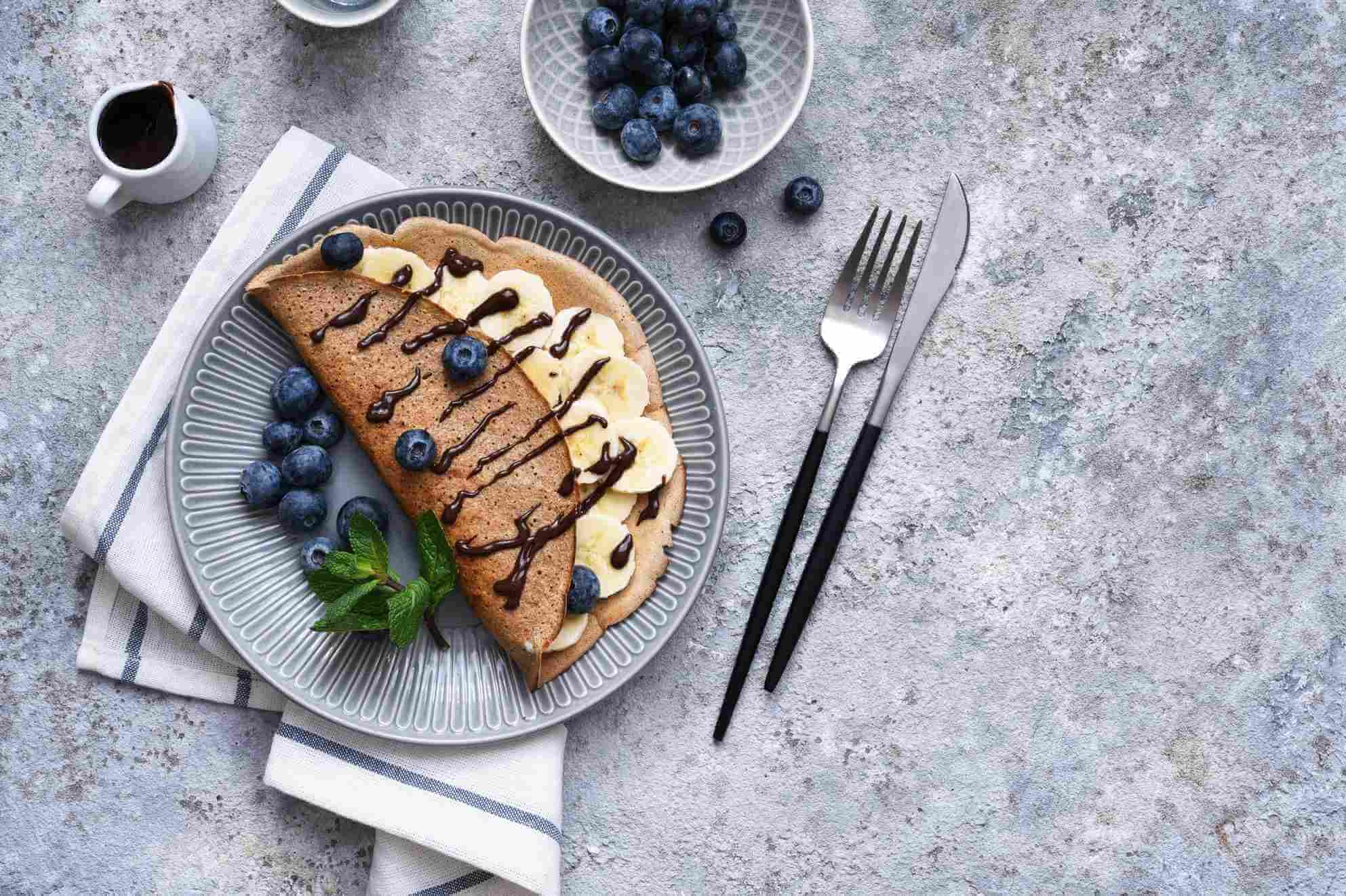 Crepe with banana, chocolate sauce and blueberries for breakfast on a stone background