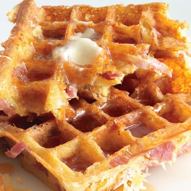 Golden brown waffles made with ham and cheese drizzled with maple syrup.
