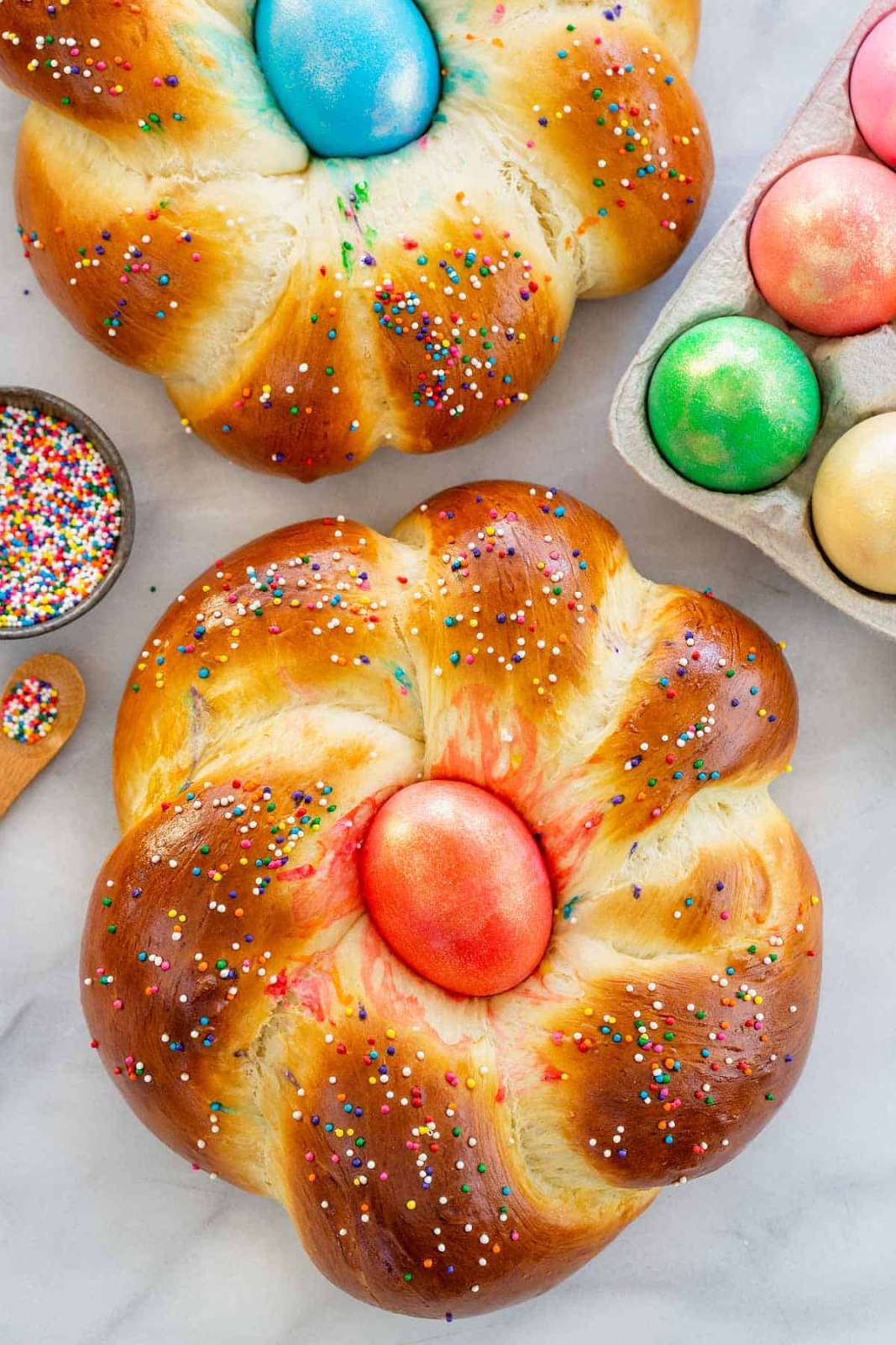 Two loaves of traditional Italian Easter bread covered in rainbow sprinkles and topped with a colored Easter egg in the center for decoration.