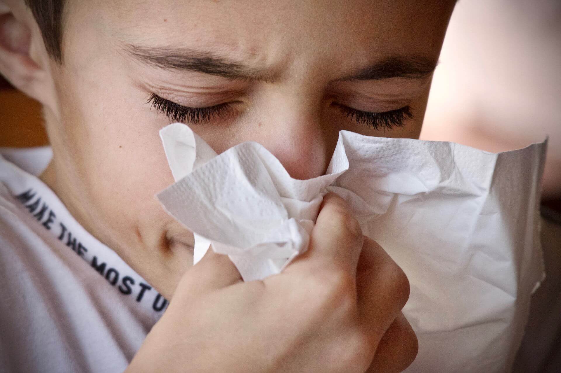 Close up of boy's face blowing up his nose with a tissue and itchy eyes