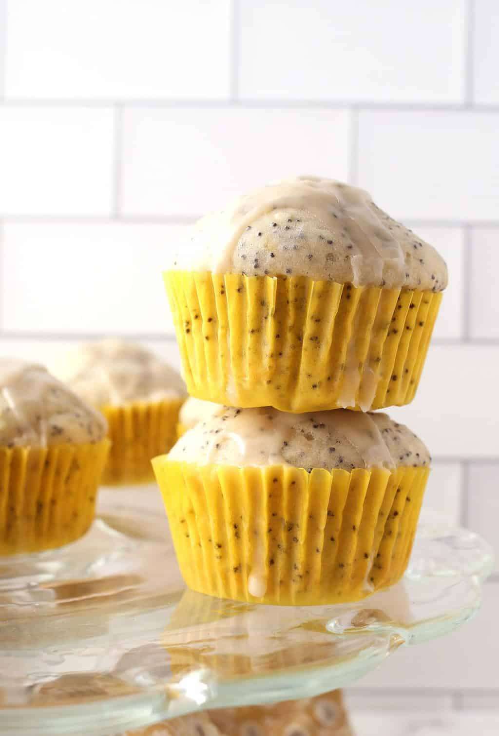 Two vegan lemon poppy seed muffins in yellow cupcake liners stacked on top of one another.