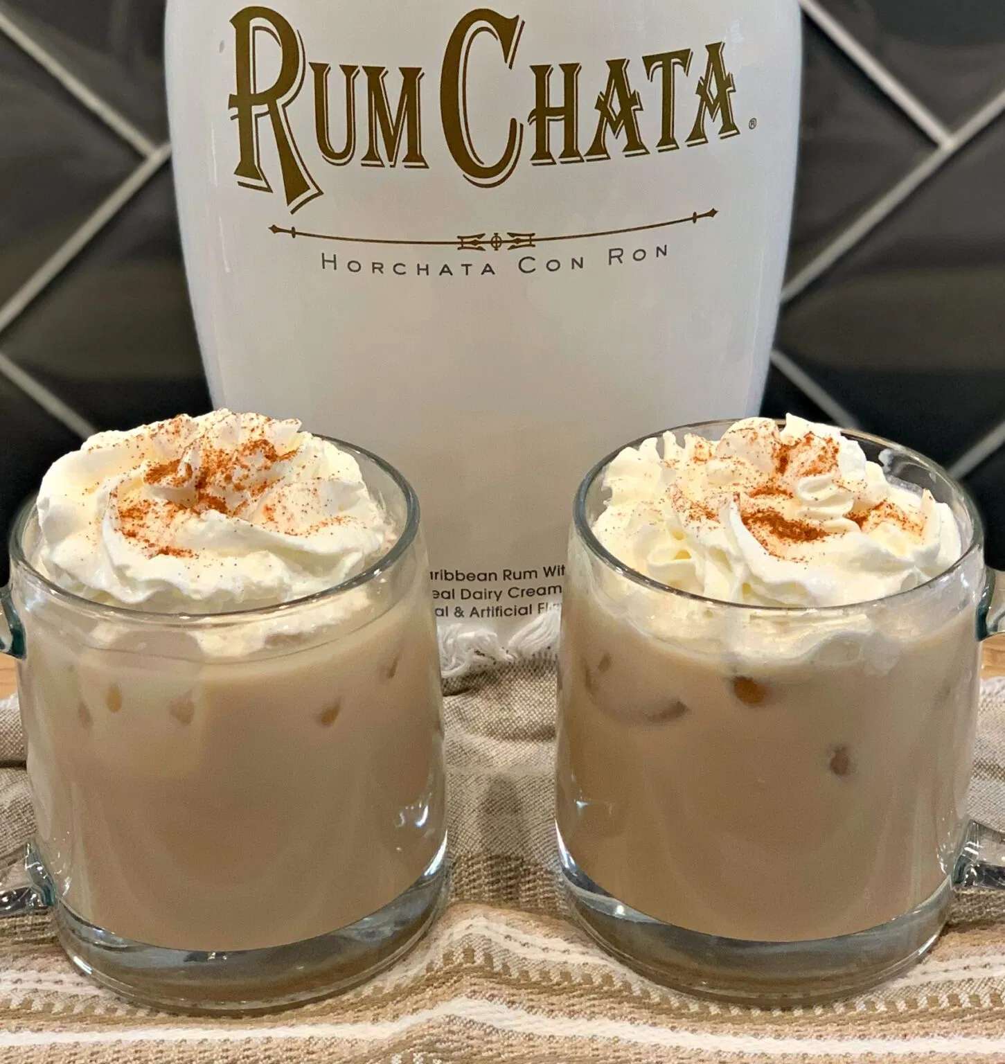 2 short glass tumblers of RumChata iced coffee, topped with whipped cream and sprinkled with ground cinnamon. 