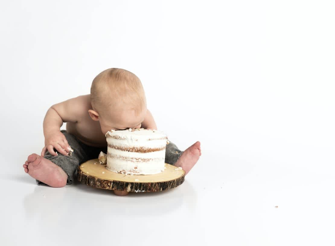 Caucasian baby face-first in a white birthday cake set on a log plate
