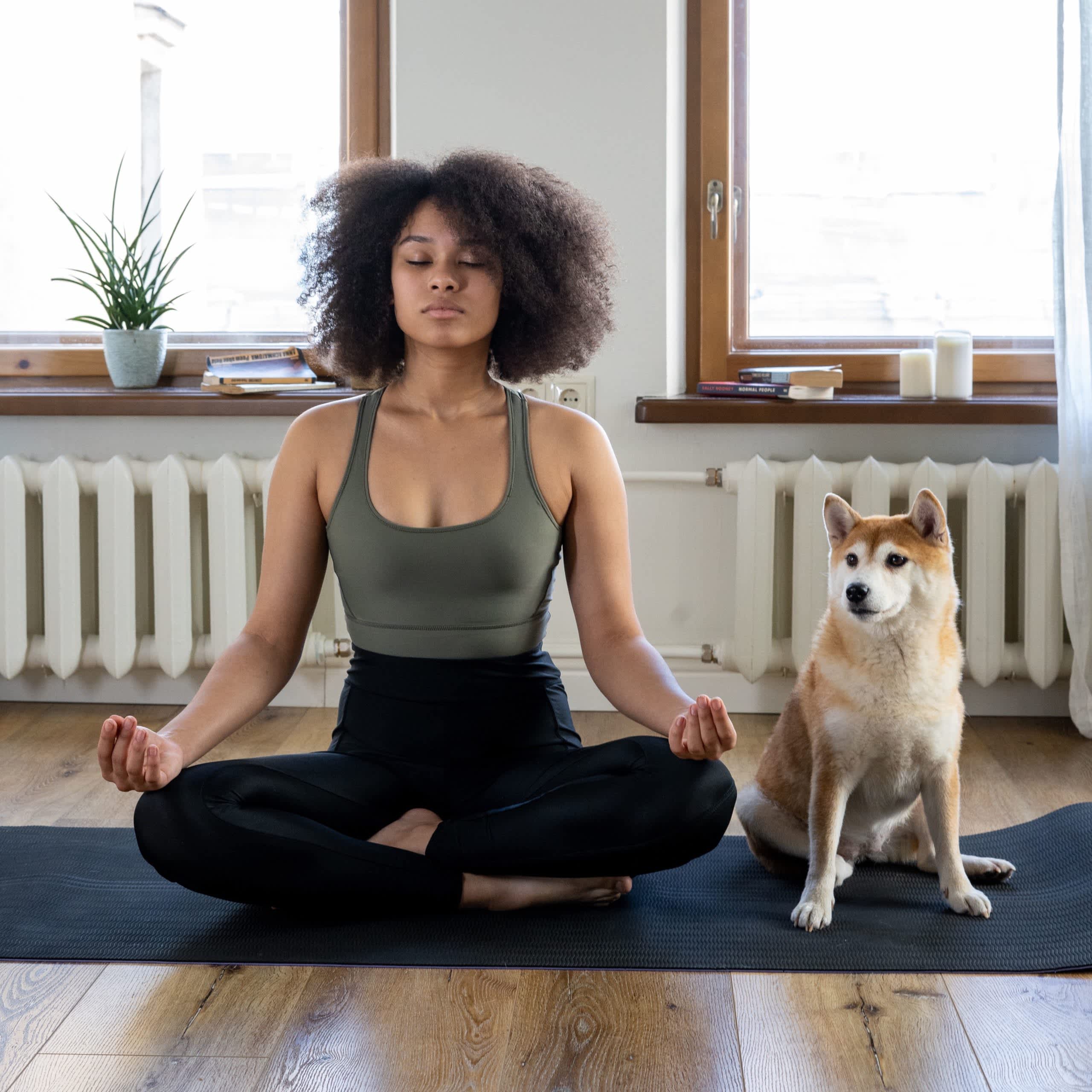 A woman in a yoga meditation pose in her house, next to her dog