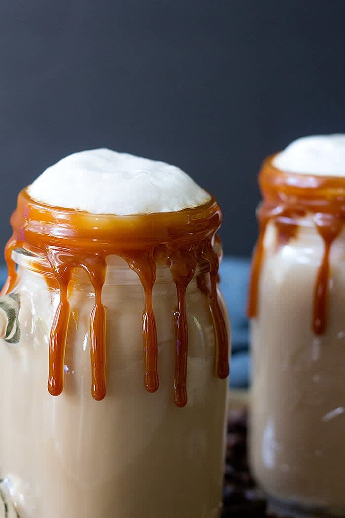 2 mason jars filled with caramel lattes with caramel dripping down sides & foam tops