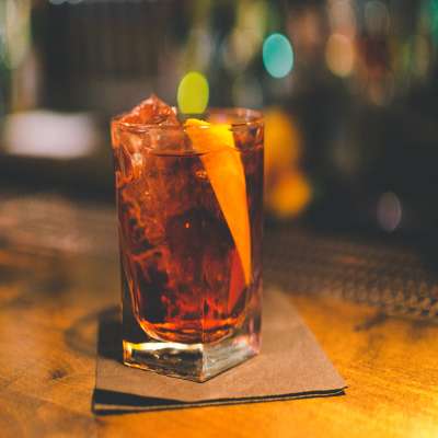 Negroni cocktail in a glass on a brown napkin and garnished with an orange peel. 