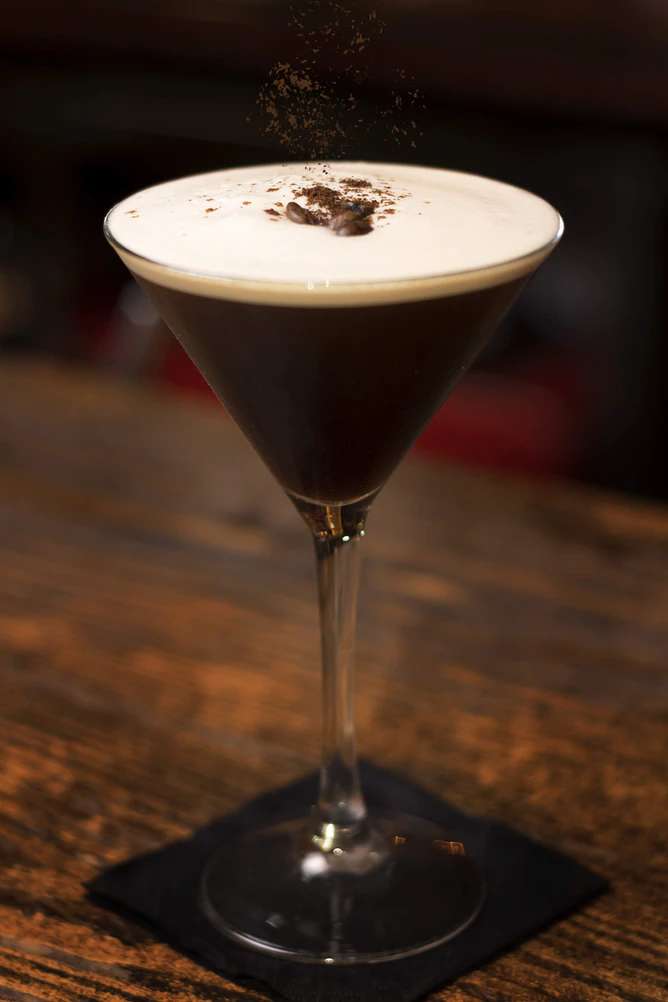 Espresso martini in a martini glass garnished with ground coffee beans.