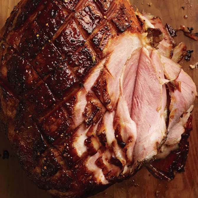 Glazed Easter ham with a brown crust, partially sliced.