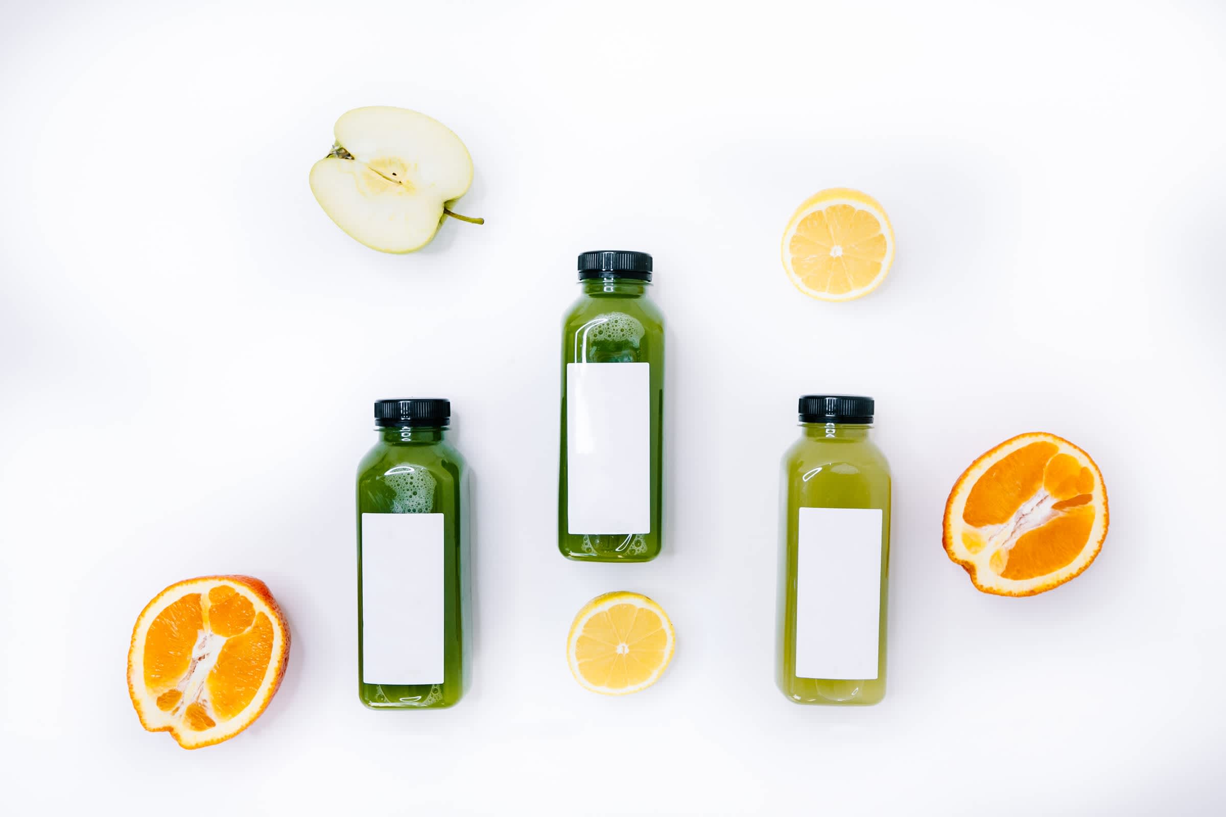 Three green juice bottles and fruits over white background
