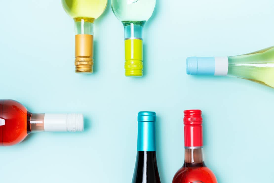 Layout frame of foil caps in different bright colors of white and rose wine bottles on blue background