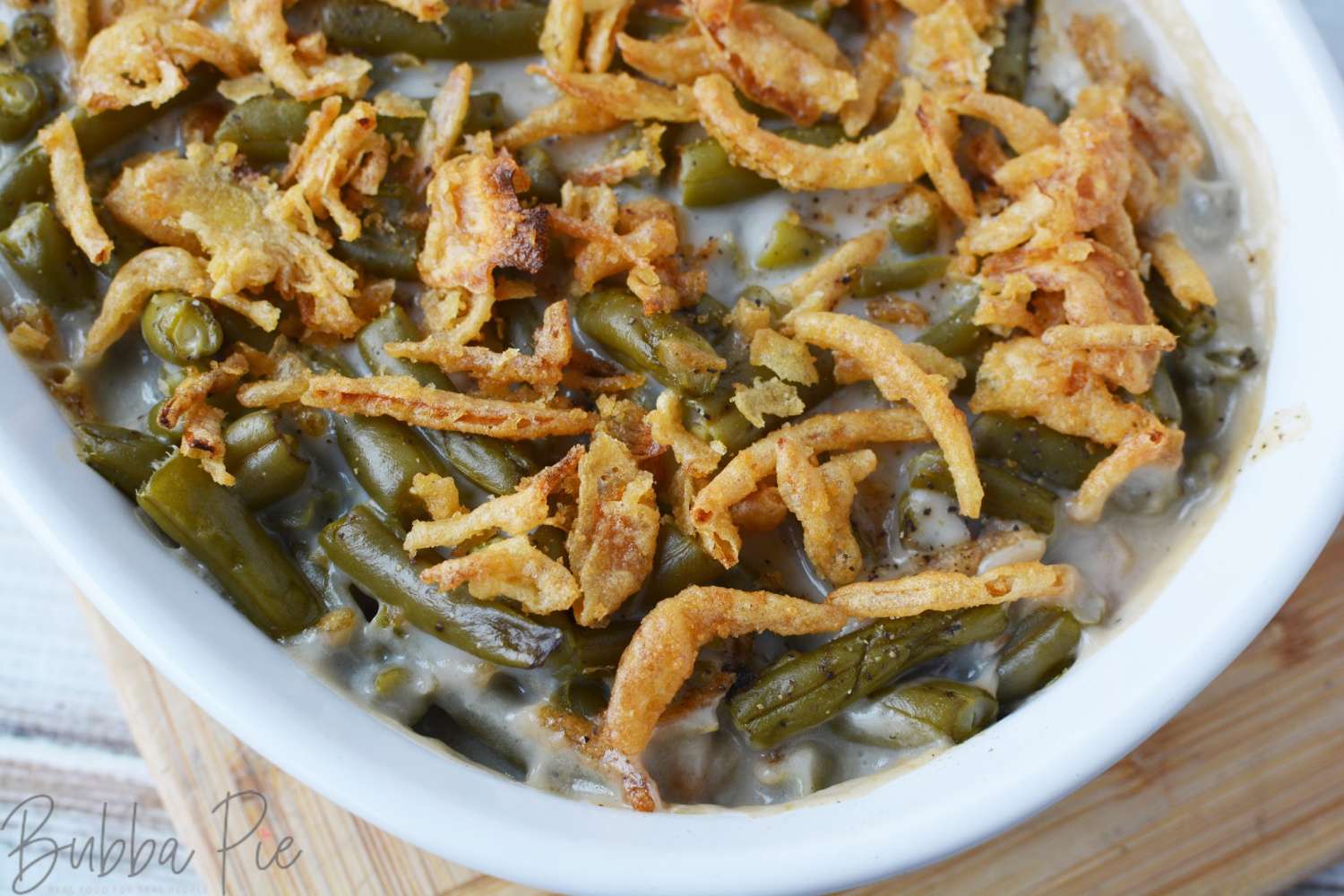 Green bean casserole with crunchy fried onions in a white casserole dish.