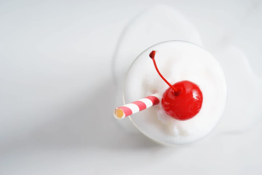 Top view  of white russian milkshake with cherry and a straw 