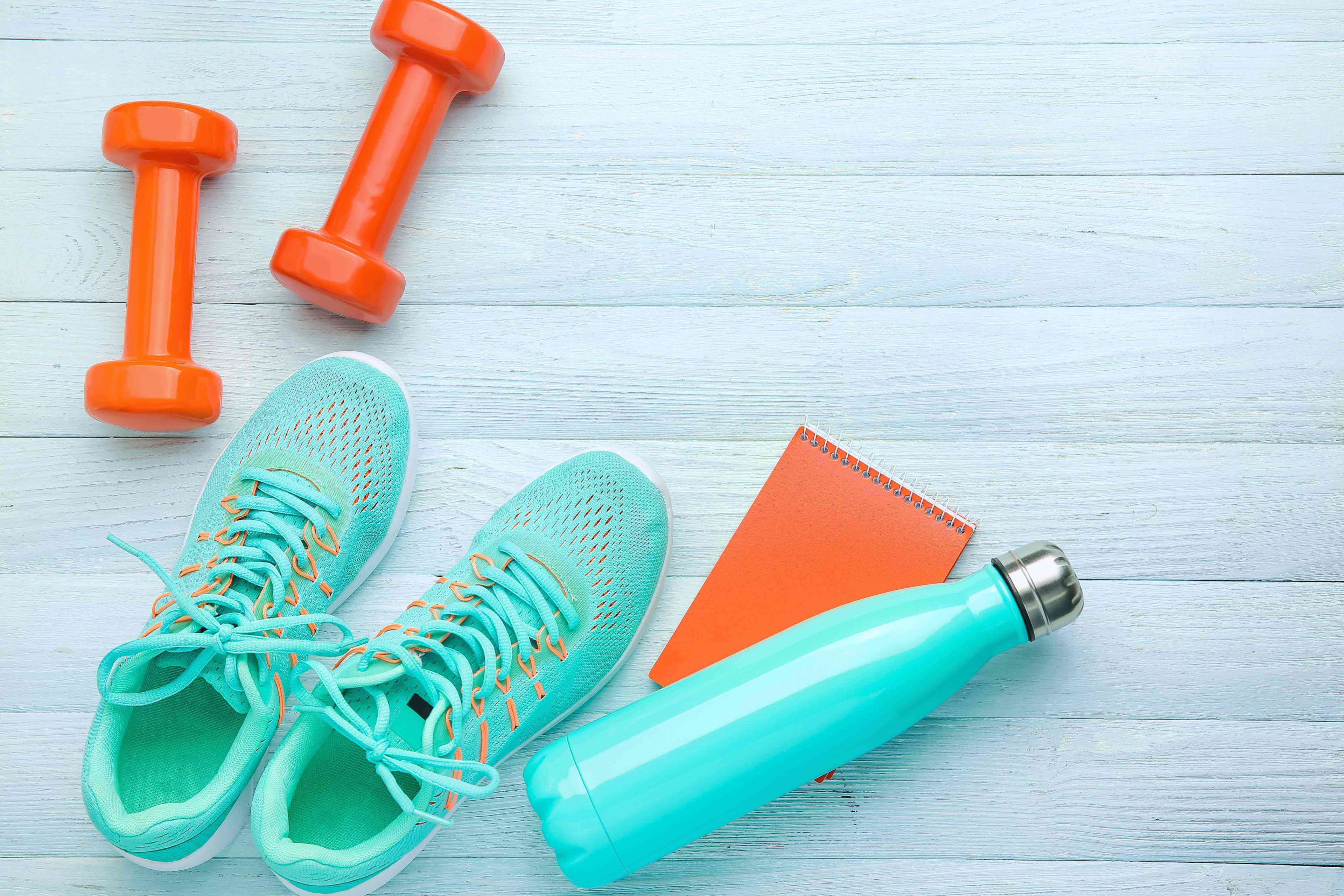 Dumbbells with notebook, shoes and bottle of water on white wooden background