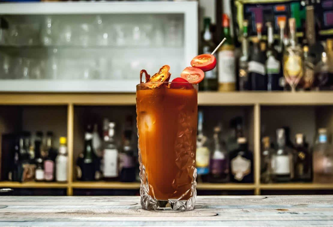 A Bloody Mary in a highball glass garnished with bacon and cherry tomatoes