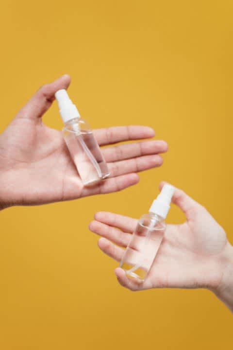 Hands with bottles of hand sanitizer against a marigold background