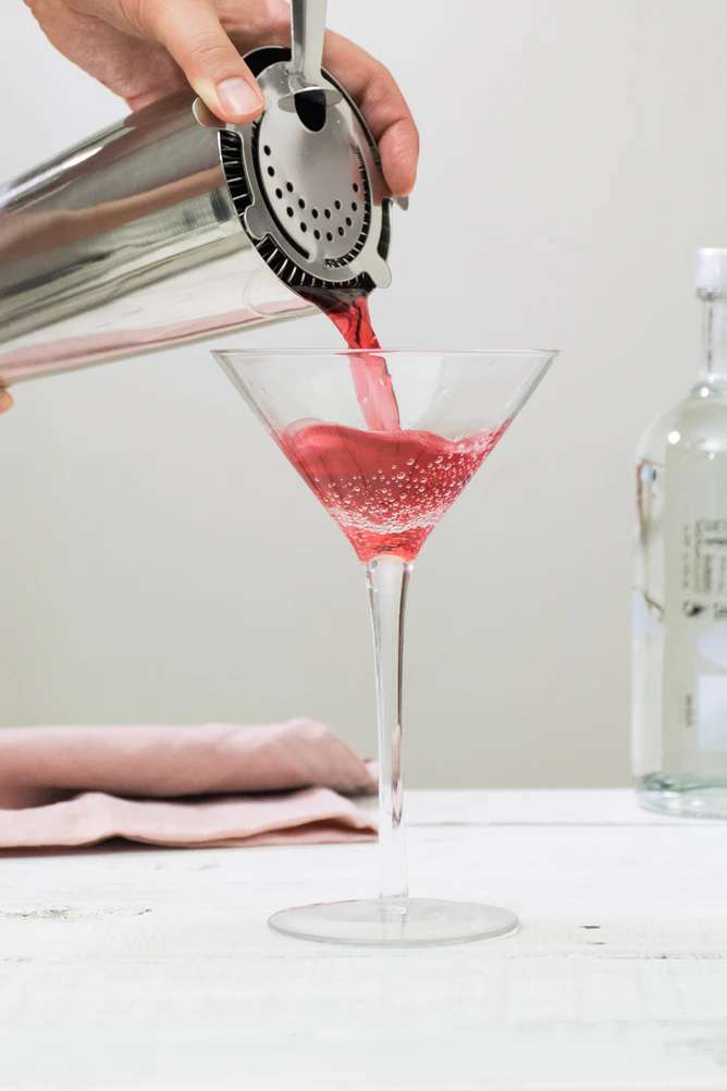 Cosmopolitan cocktail being poured through a strainer into a martini glass.