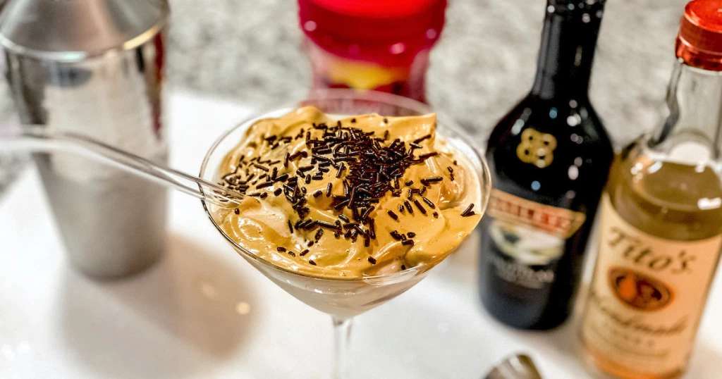 Dalgona Coffee Martini in martini glass, bottles of Baileys Irish Cream and Tito’s Vodka