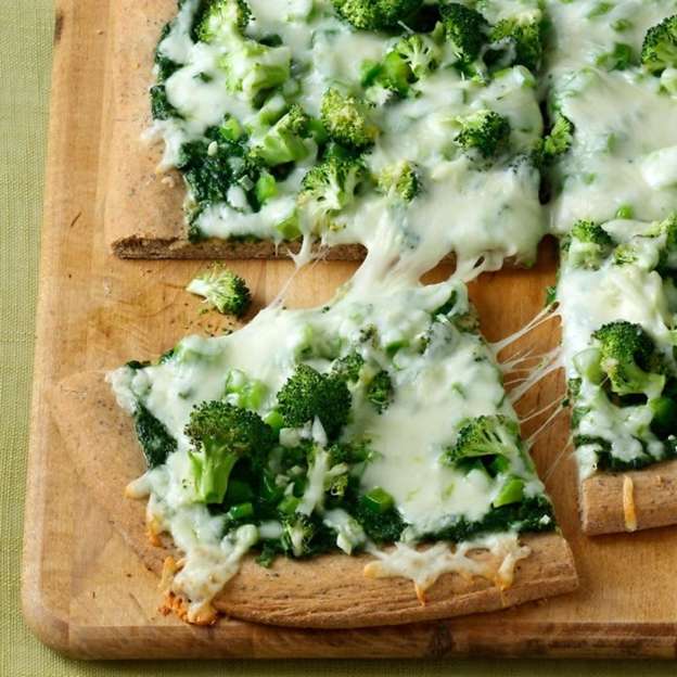 Close up of pesto veggie pizza on a cutting board