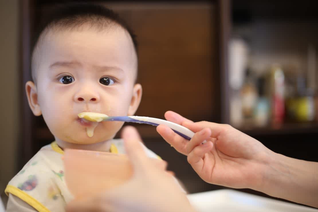 Asian baby being spoon fed a baby food puree 