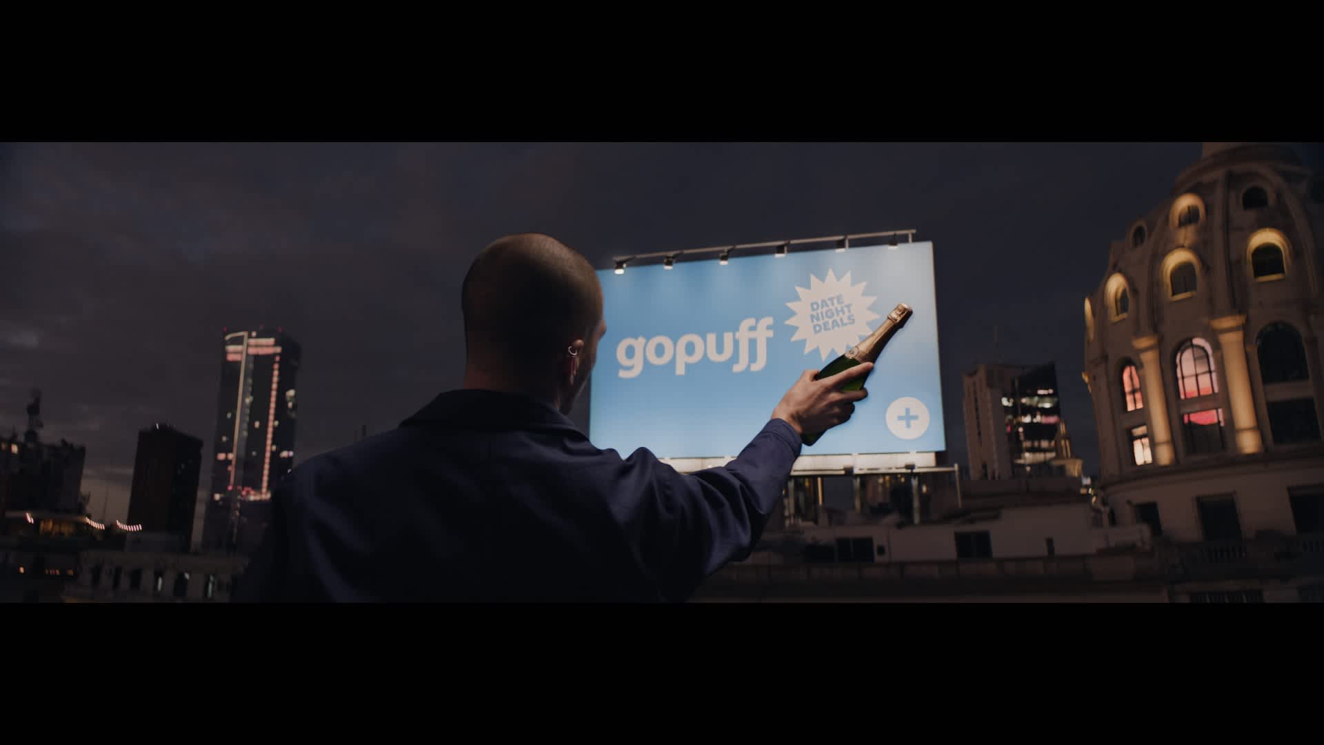 Shot from Gopuff's "Bring The Magic" film. Protagonist plucks a bottle of bubbly from a billboard. 