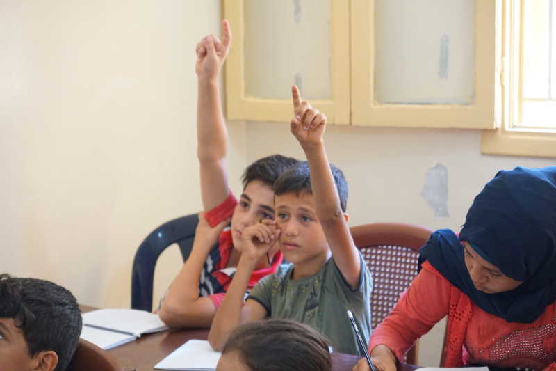 Två pojkar räcker upp handen i en skolsal i Libanon. 