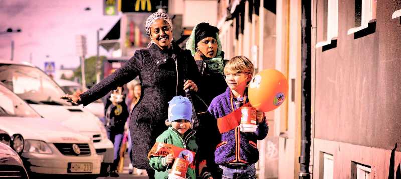 Två kvinnor och två barn går med bössor och ballonger med Världens Barn logotyper. 