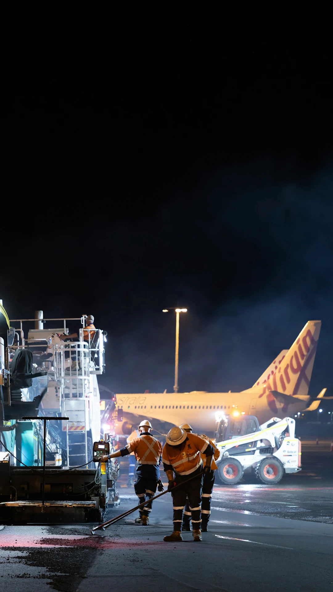 Workers repair tarmac near airplane at night