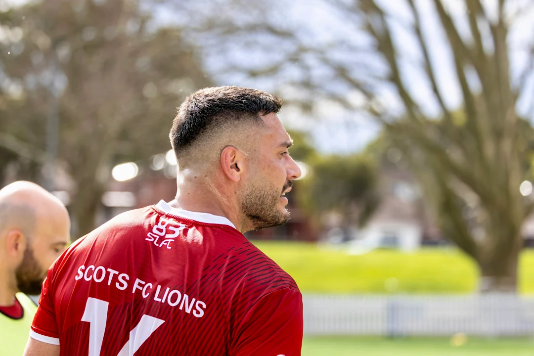 Man in red scots fc lions jersey on field.