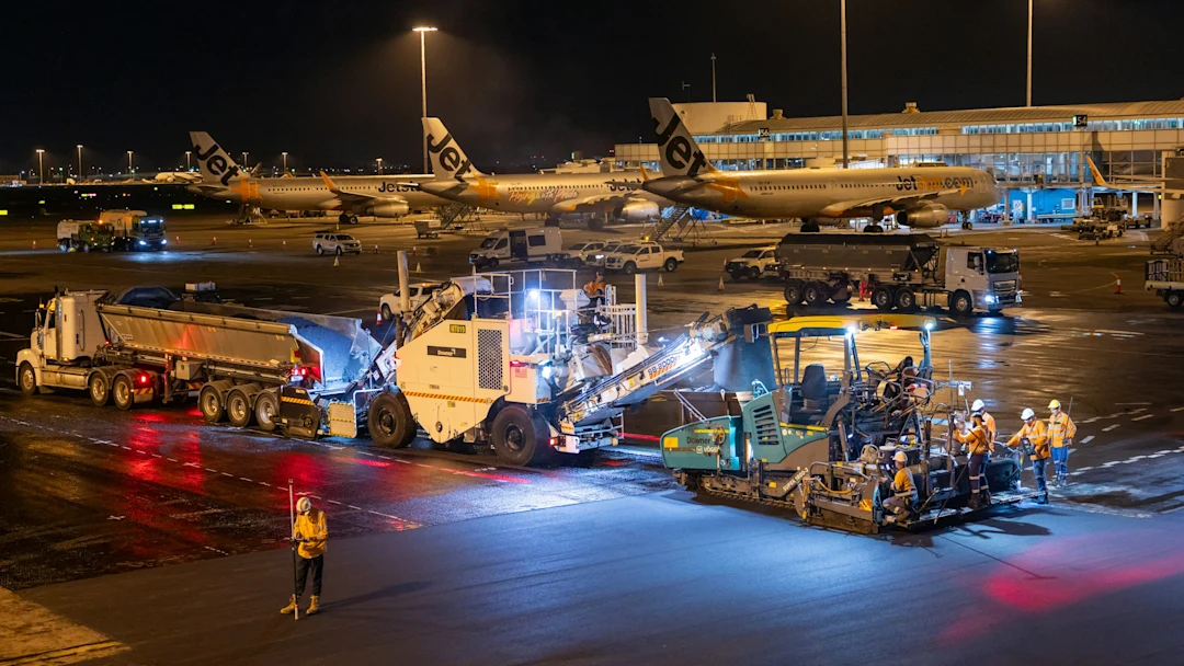Airport tarmac resurfacing work at night with machinery and workers.
