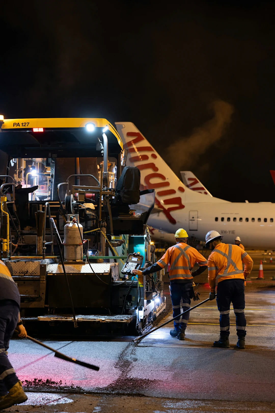Workers paving tarmac at night near airplanes