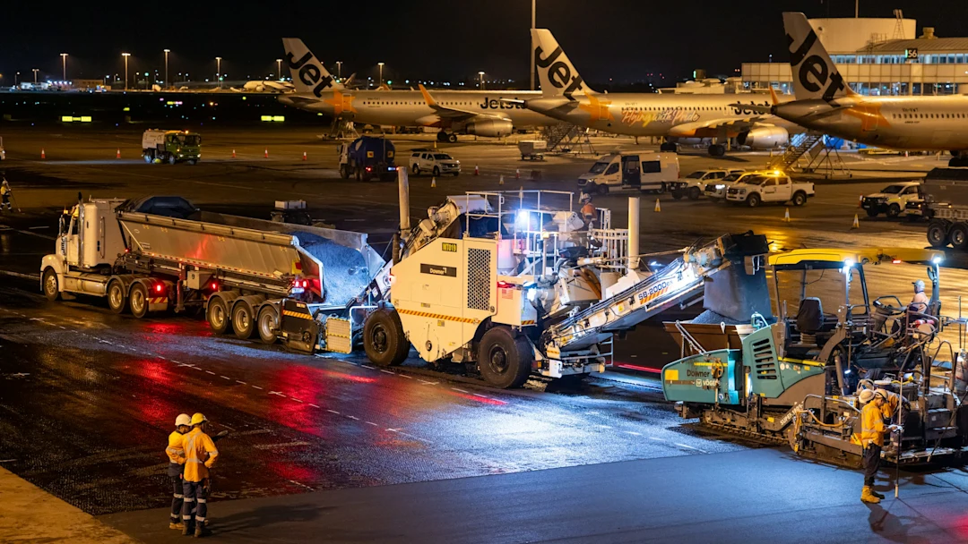 Airport runway resurfacing at night with heavy machinery.