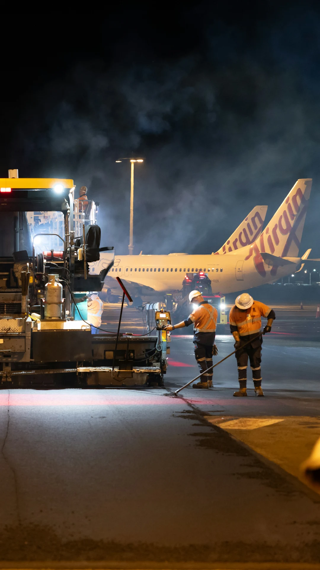 Airport workers paving tarmac near virgin australia airplanes at night