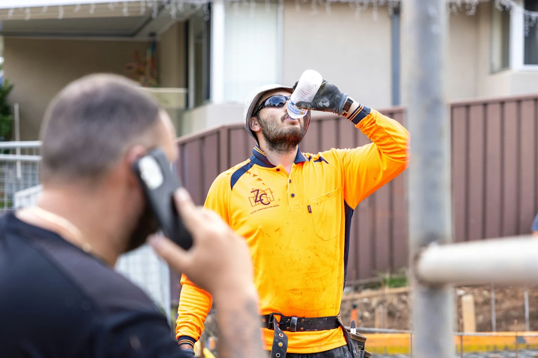 A construction worker drinks water while another talks.
