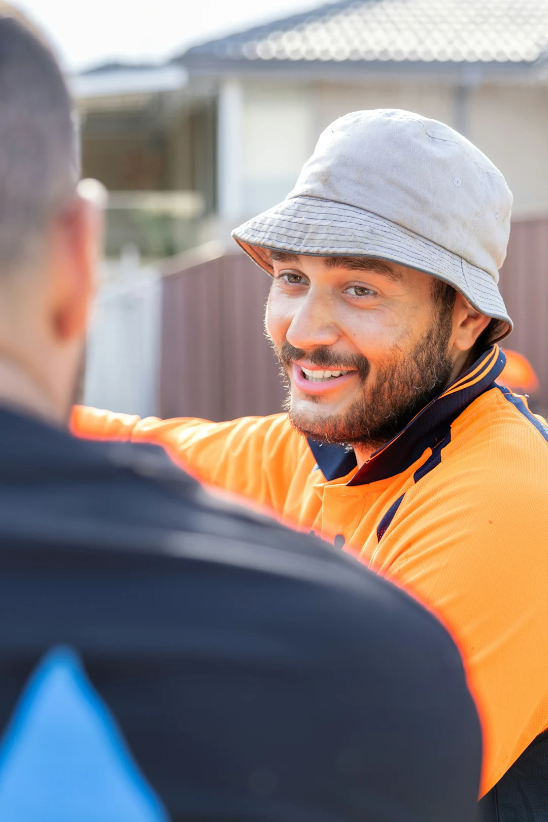 Man in orange shirt smiles at another.