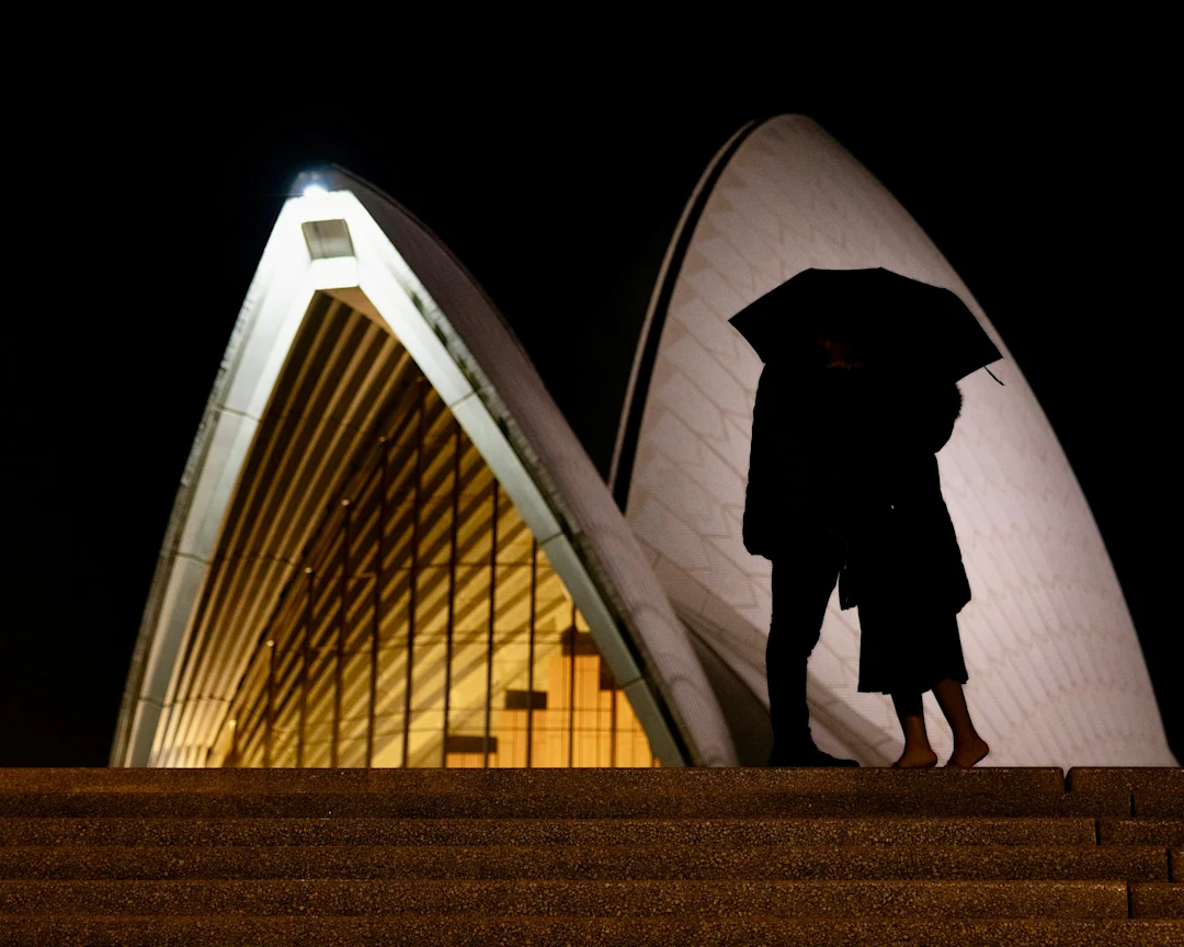 Couple under umbrella at night near building.