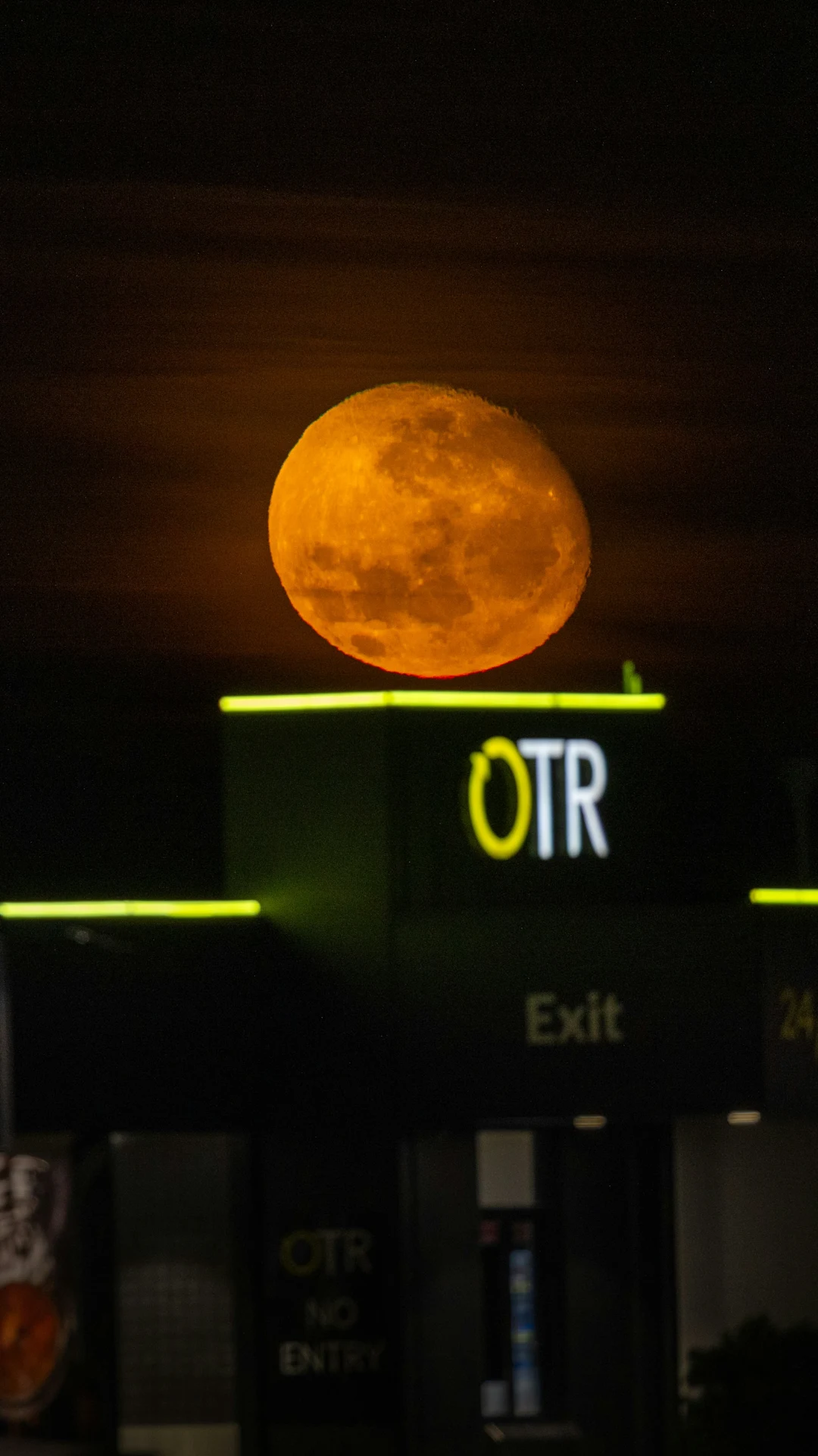Orange moon hovering over a building exit sign