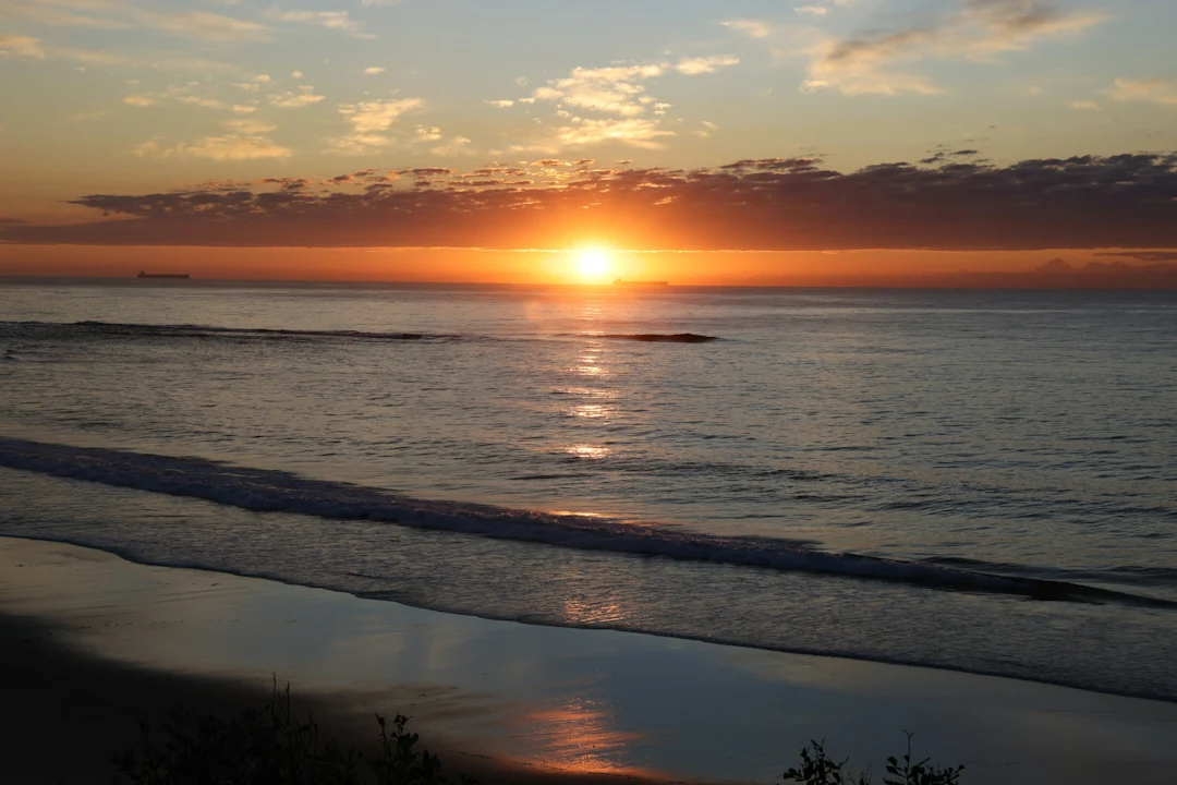The sun is setting over the ocean on the beach