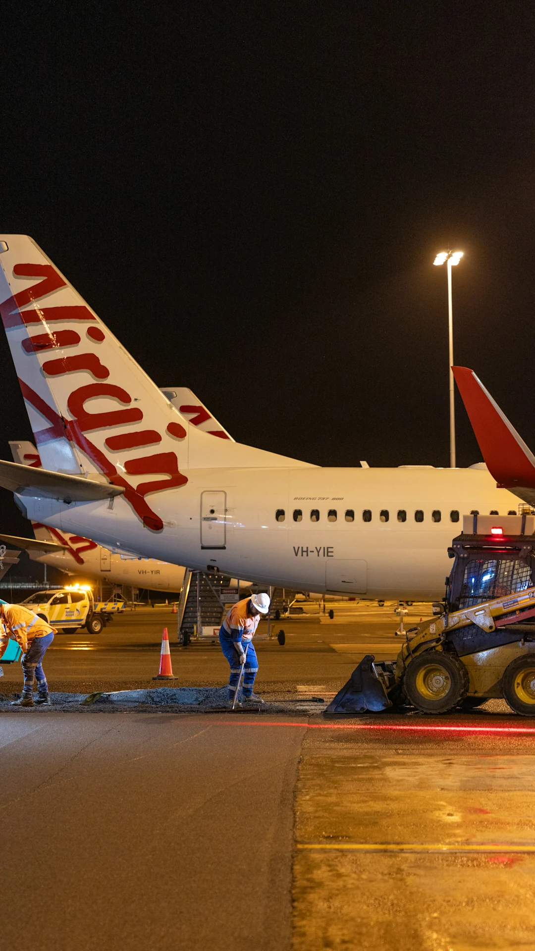 Airport workers repair tarmac near virgin australia airplanes at night.