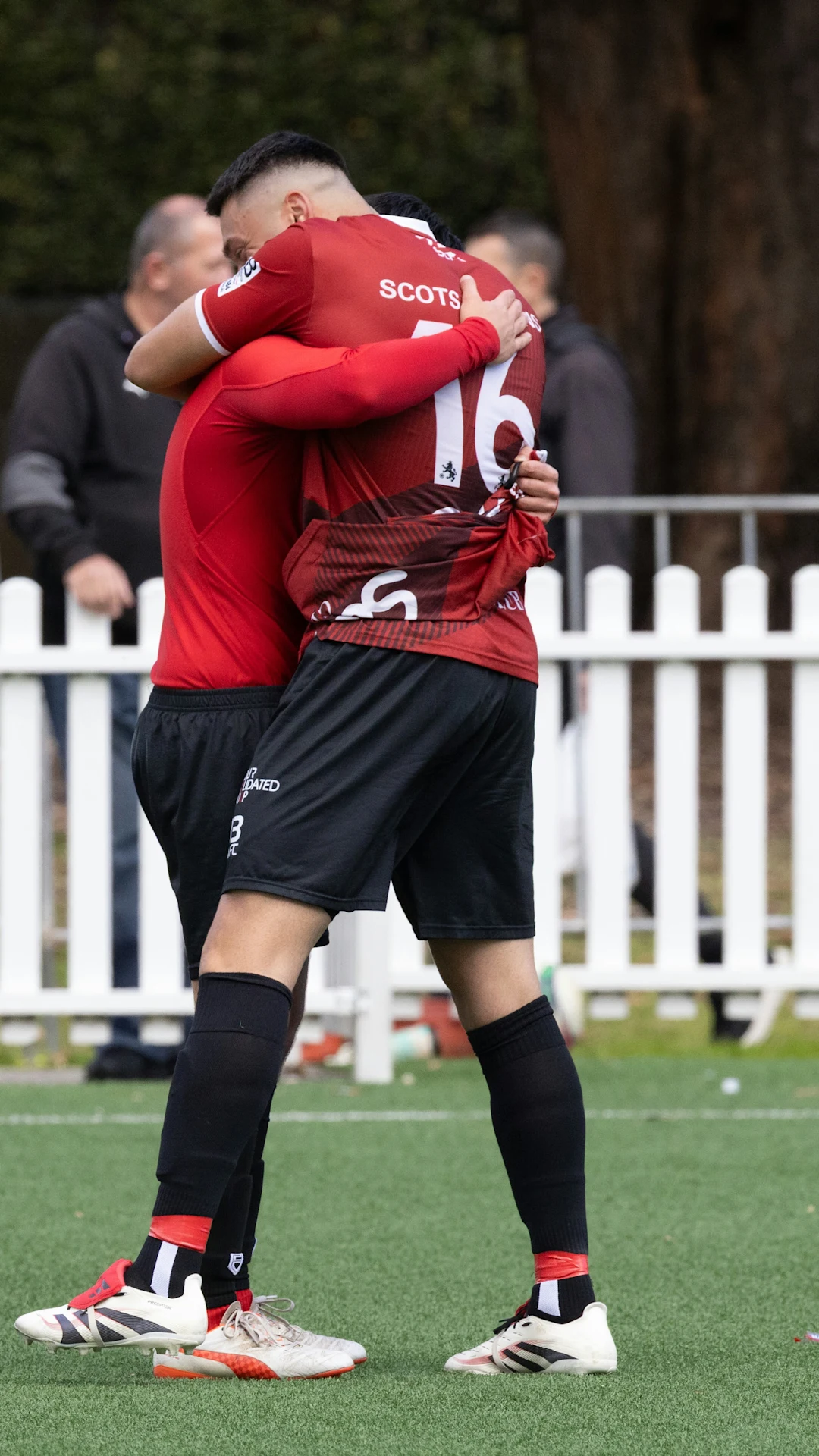 Two soccer players in red uniforms hugging on field.