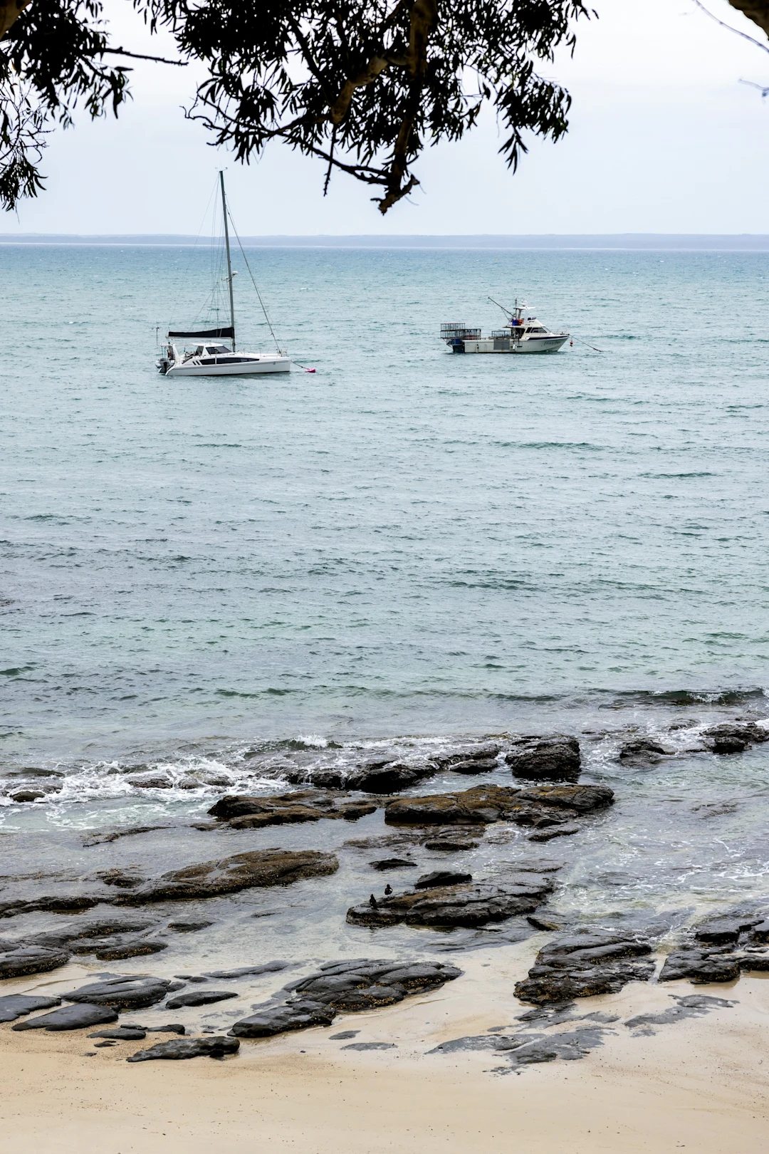 Two boats sail on the ocean near rocky shore.