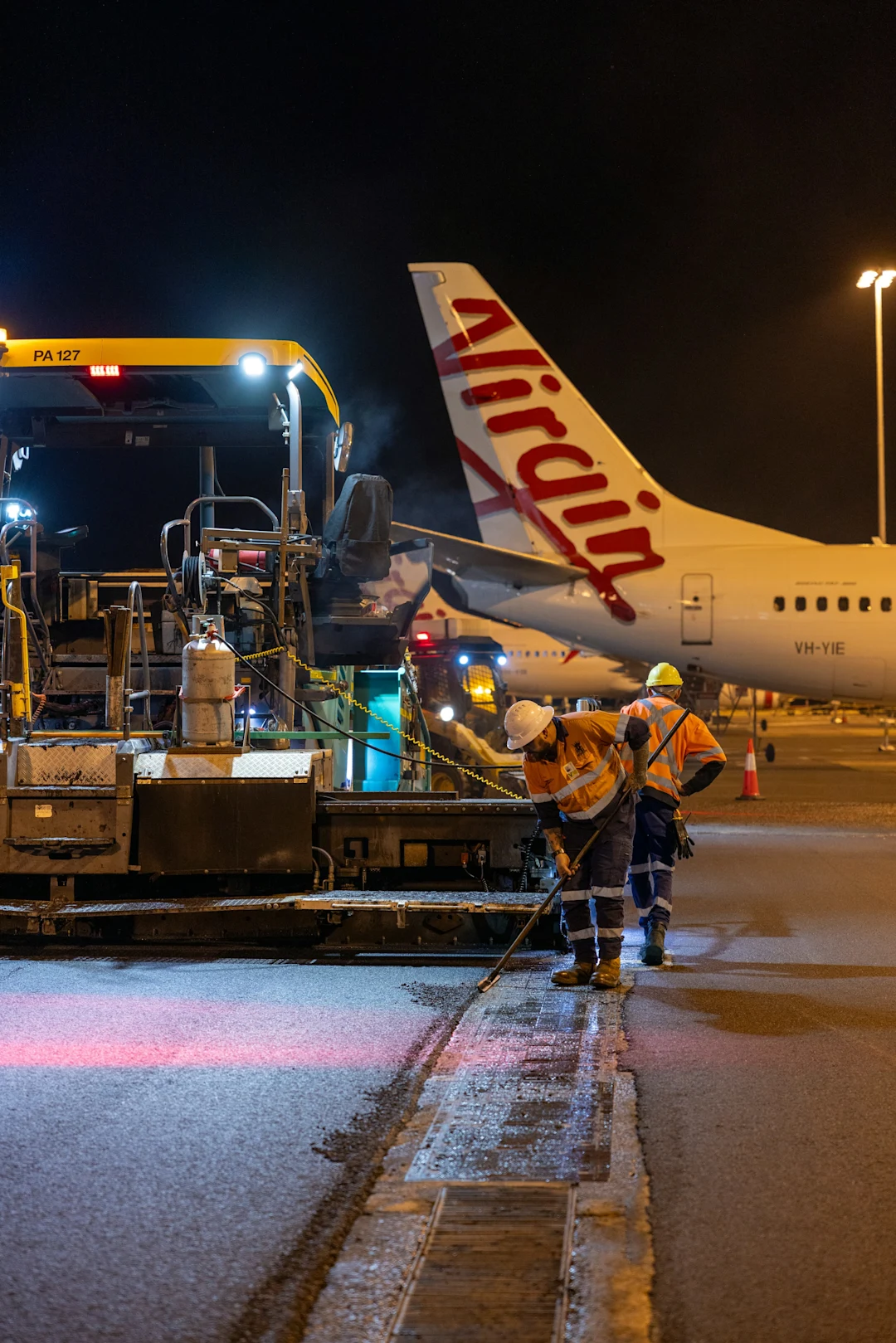 Workers repaving tarmac near virgin australia airplane at night
