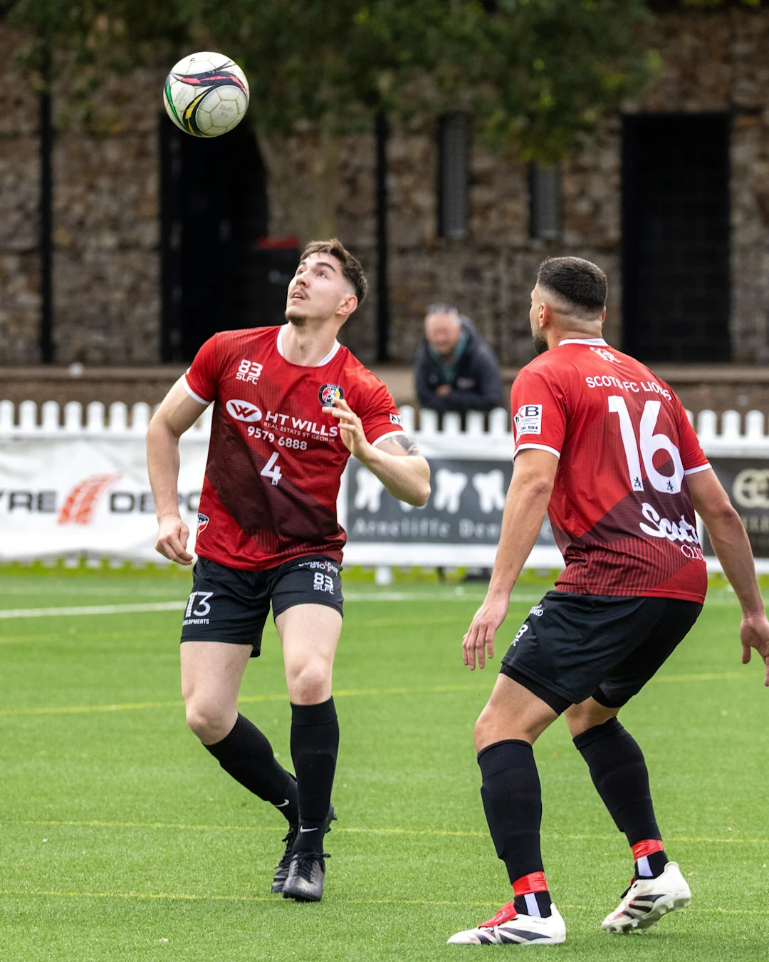 Two soccer players in red jerseys heading ball