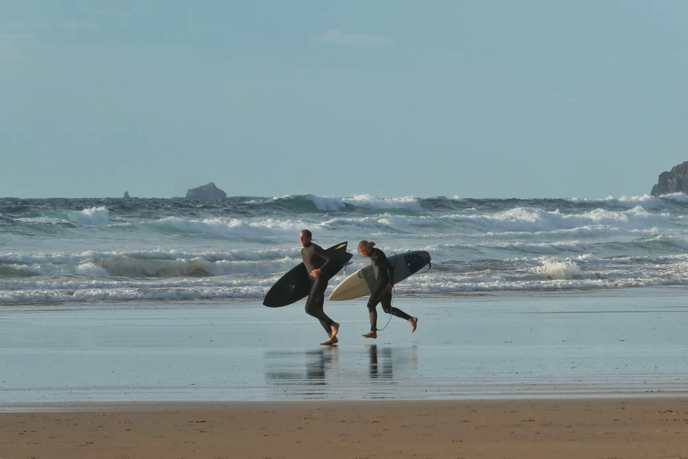 A man and a woman running with their surfboards along the sea