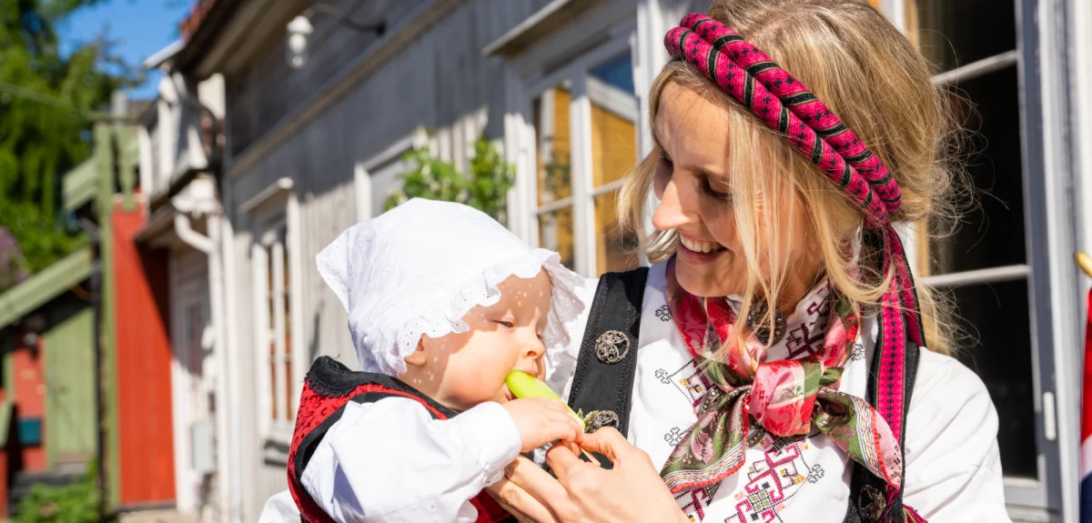 A baby dressed in the Norwegian national dress eating an ice cream