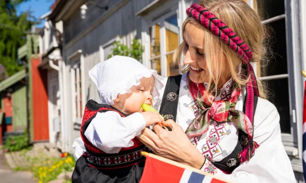 A baby dressed in the Norwegian national dress eating an ice cream