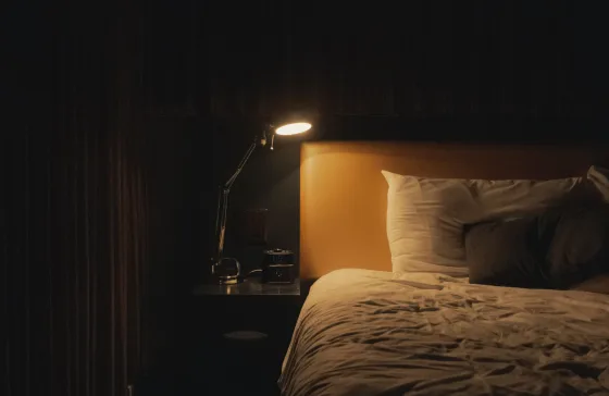 A bedside lamp illuminates a dark hotel room