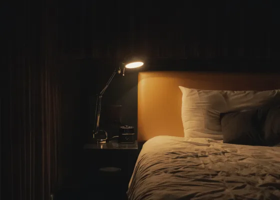 A bedside lamp illuminates a dark hotel room